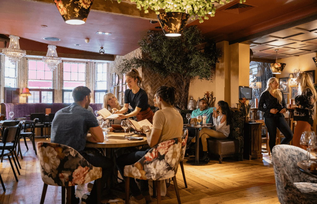 A waitress talking through a menu ith a group of seated diners