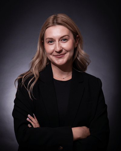 Zsofia Karnok standing ewith arms folded, smiling in a black suit jacket